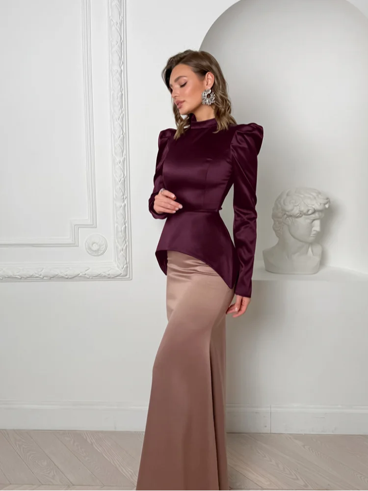 Woman wearing a burgundy top and brown skirt in a white room.