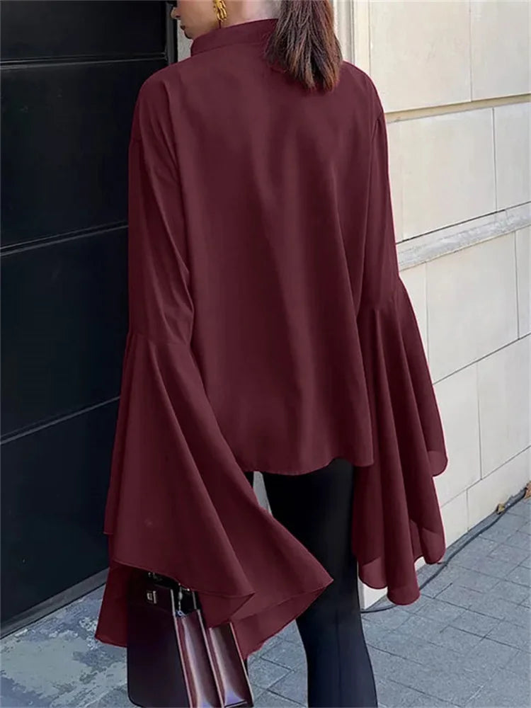 Person wearing a burgundy blouse with long sleeves and a high collar, standing against a tiled wall.