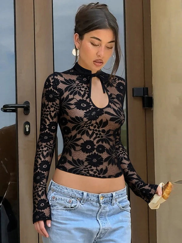 Woman wearing a black floral lace top and light blue jeans standing in front of a door.