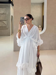Woman in a white dress taking a mirror selfie in an indoor setting.