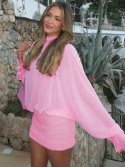 Woman wearing a pink outfit standing outdoors with a stone wall and plants in the background