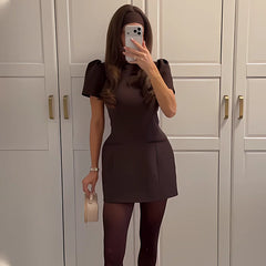 Person wearing a brown dress taking a mirror selfie in front of white cabinets.