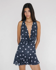 Woman wearing a navy blue dress with white polka dots on a plain background