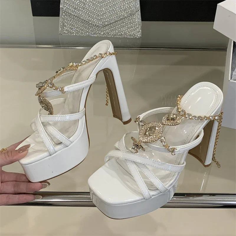 White high-heeled shoes with gold embellishments on a reflective surface.