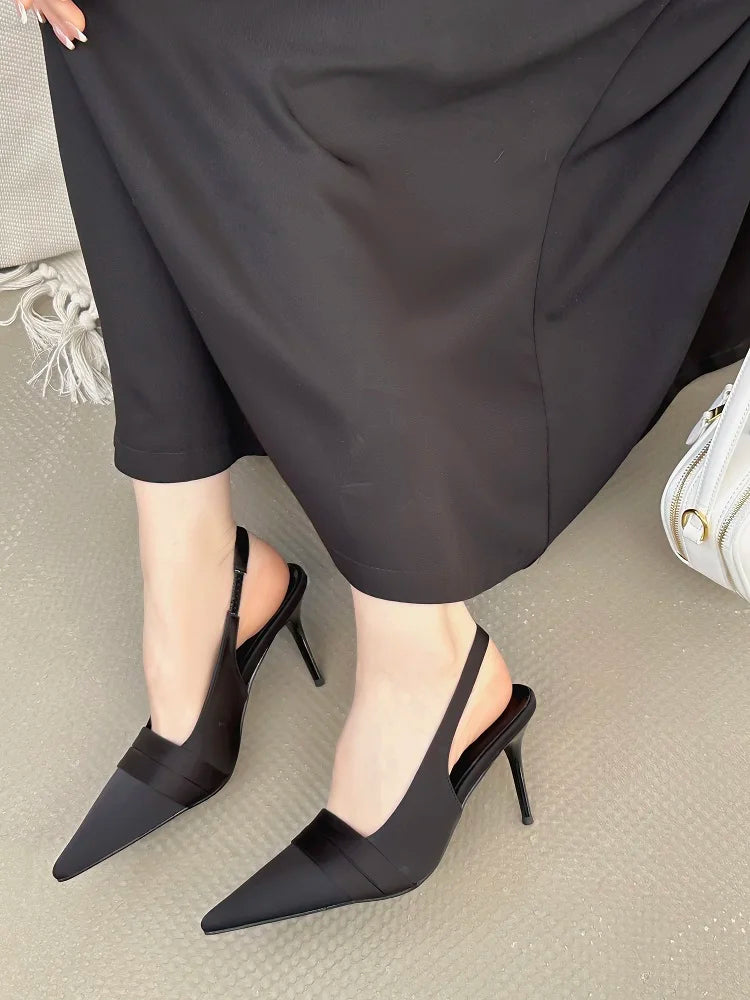 Black heeled shoes worn with a black outfit on a neutral background