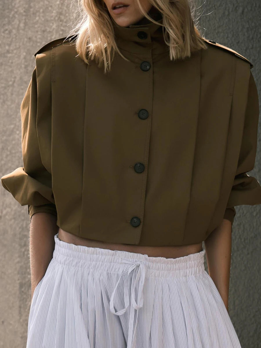 Person wearing a brown cropped jacket with buttons and white pants against a neutral background