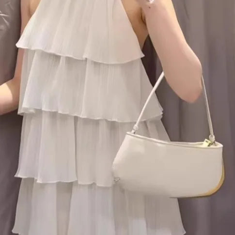 Person wearing a white dress holding a beige handbag against a neutral background