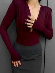 Person wearing a burgundy long-sleeve top and dark gray skirt against a gray background