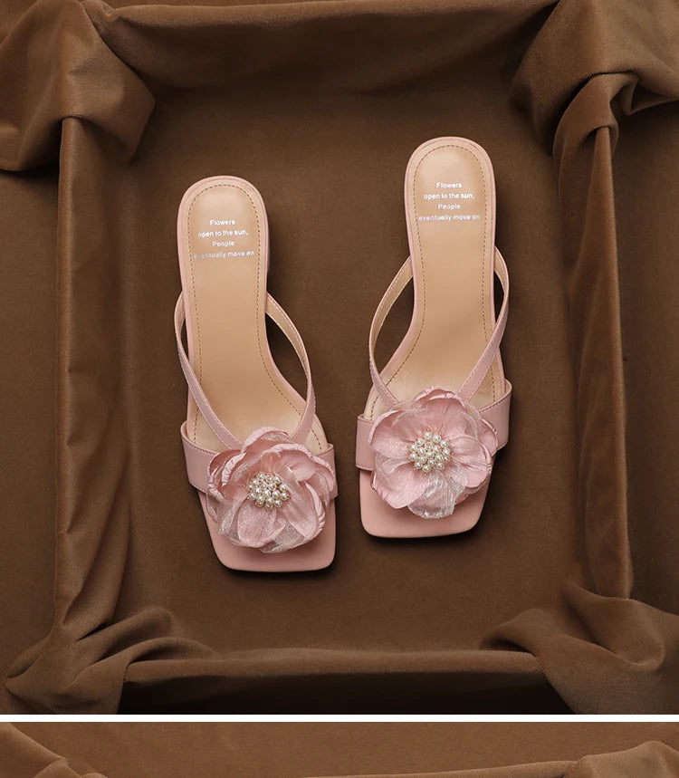 Pair of pink high-heeled sandals with floral decorations on a brown fabric background