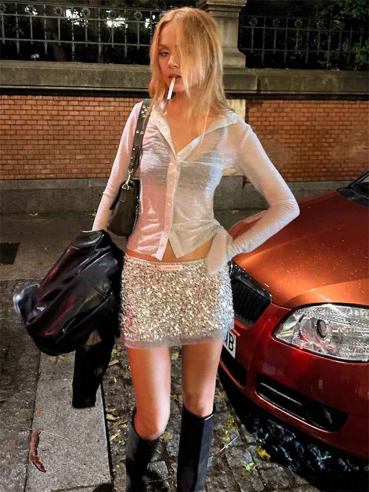 Woman in a sequin skirt standing next to a red car on a street.