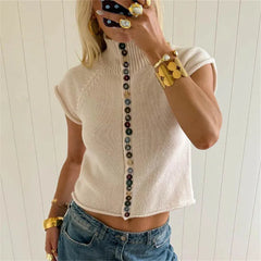 Beige knitted top with button details worn by a person against a white background