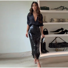 Woman in black sequin pants and top standing in front of a shoe rack with various shoes.