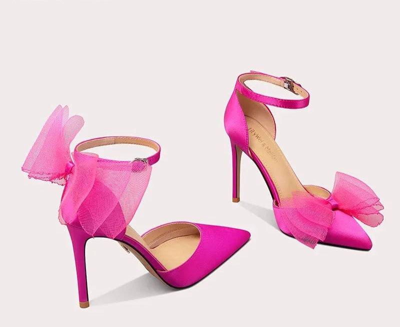 Pink high-heeled shoes with decorative bows on a light gray background