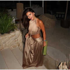 woman smiling in a gold halter neck crop top and matching flowing maxi skirt, holding a green clutch
