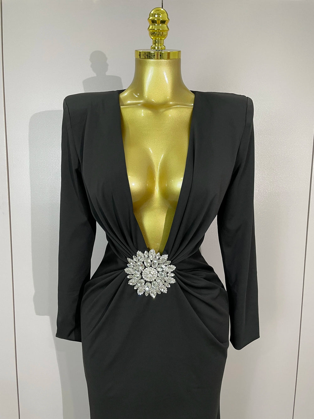 Black dress with a large brooch on a mannequin against a white background