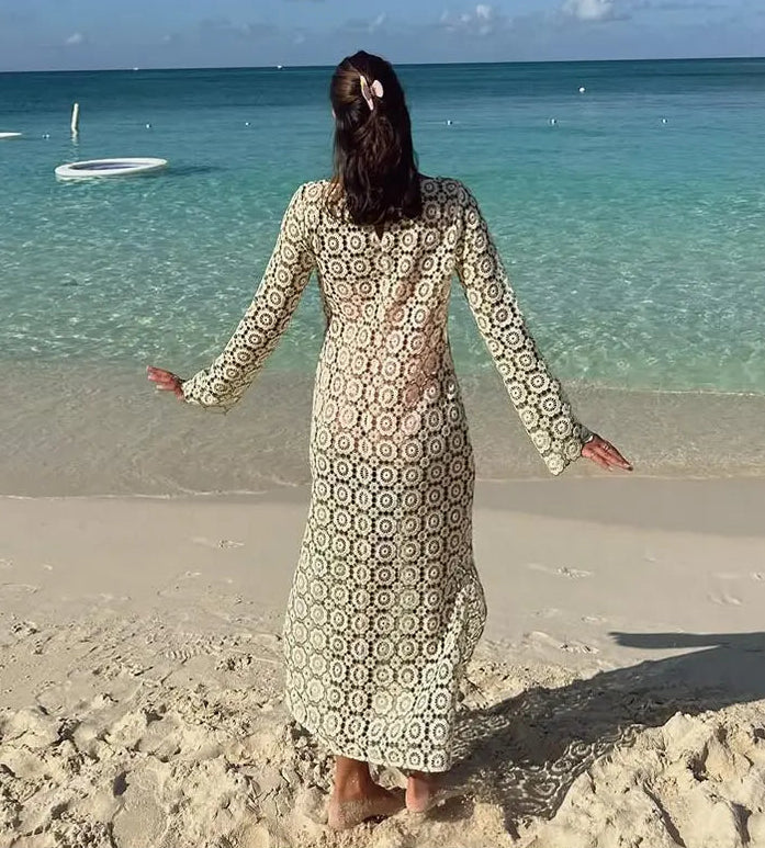 Woman in a patterned dress standing on a beach with clear blue water and sky.