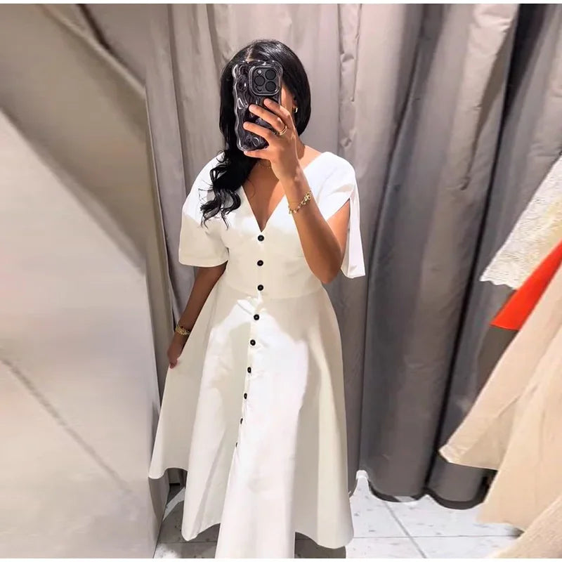 Person wearing a white dress with black buttons in a fitting room.
