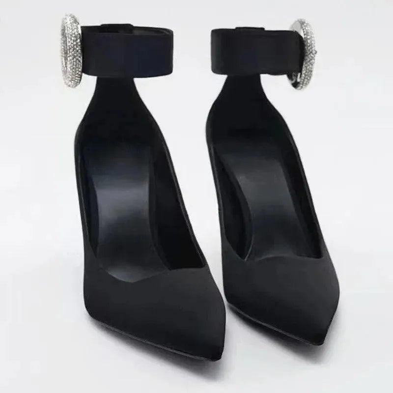 Pair of black pointed toe pumps with rhinestone ankle strap buckle.