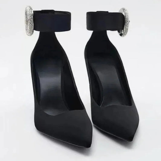 Pair of black pointed toe pumps with rhinestone ankle strap buckle.