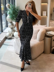 Woman taking a mirror selfie wearing a black and white polka dot dress in a modern living room.