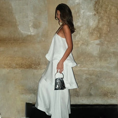 Woman in a white dress holding a black handbag against a textured wall.