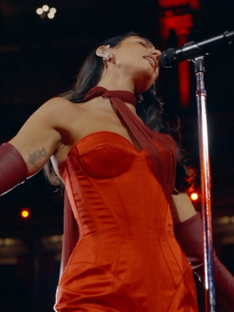 Person in a red dress singing into a microphone on stage at night.