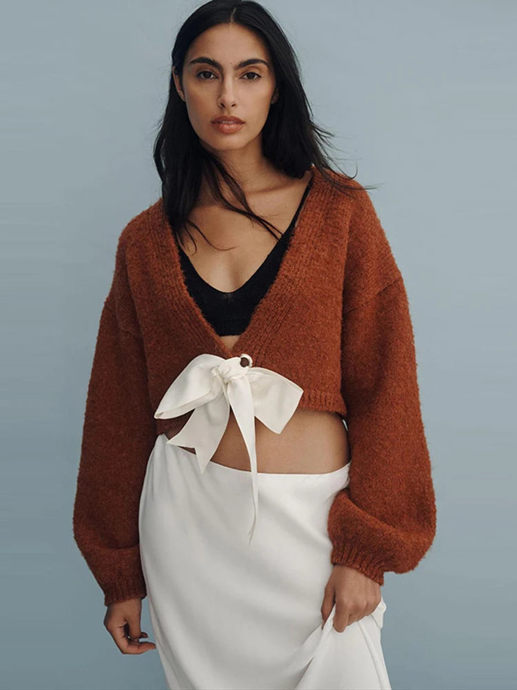 Woman wearing a brown cardigan over a black top with a white skirt on a gray background