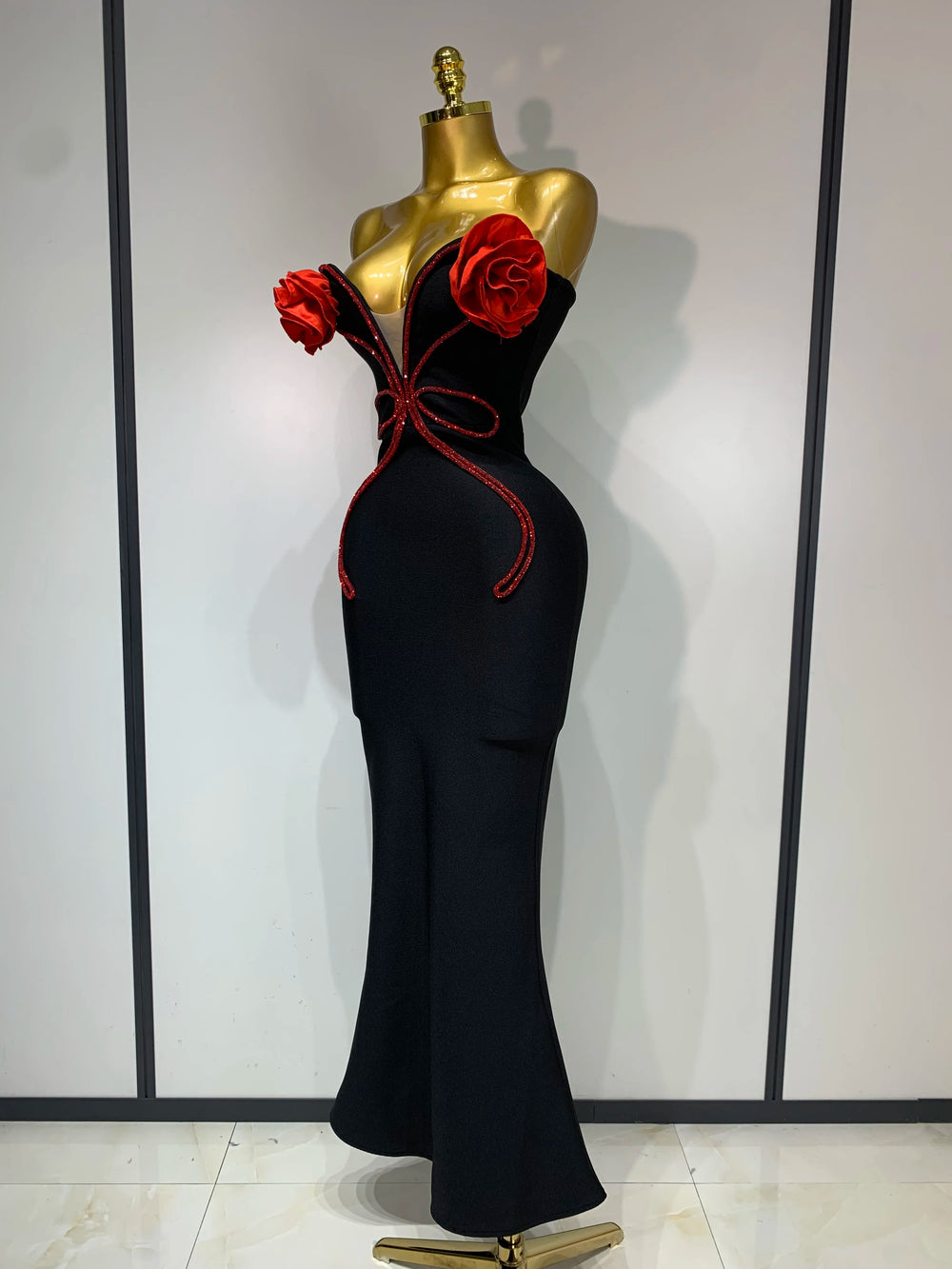 Black evening gown with red floral accents on a mannequin against a white wall.