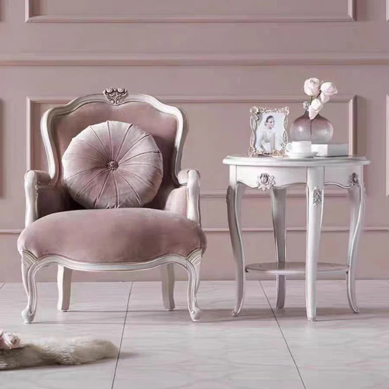 Pink armchair with decorative pillow in a stylish room with a side table and decor items.