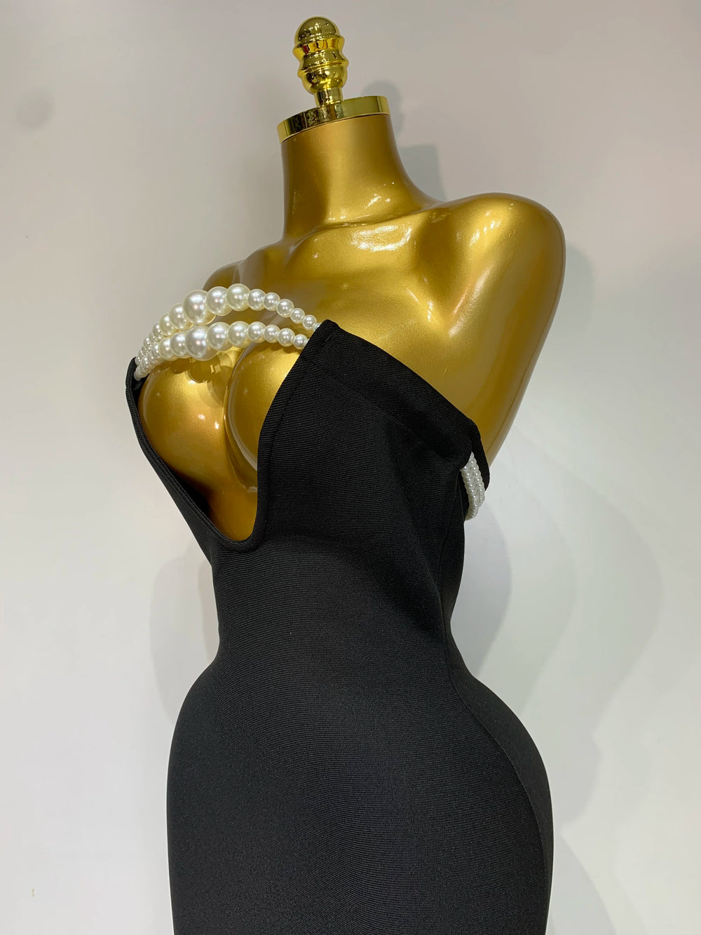 Mannequin wearing a black dress with pearl-like embellishments on a white background