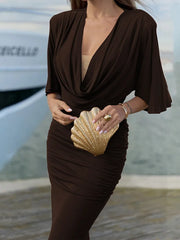 Woman in a brown dress holding a gold clutch with a blurred background