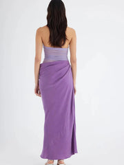 Woman wearing a purple strapless dress with a slit on a white background