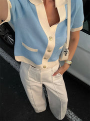 Person wearing a light blue and white cardigan with beige pants, standing next to a car.