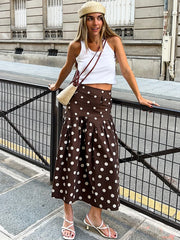 Woman in a white top and brown polka dot skirt standing on a city street.