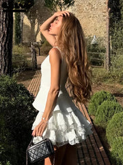 Woman in a white dress standing outdoors with trees and a stone wall in the background