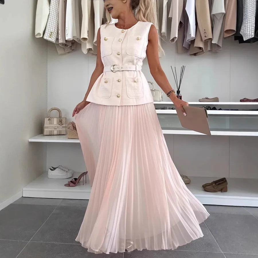 Woman wearing a white sleeveless top with buttons and a long light pink pleated skirt in a clothing store.