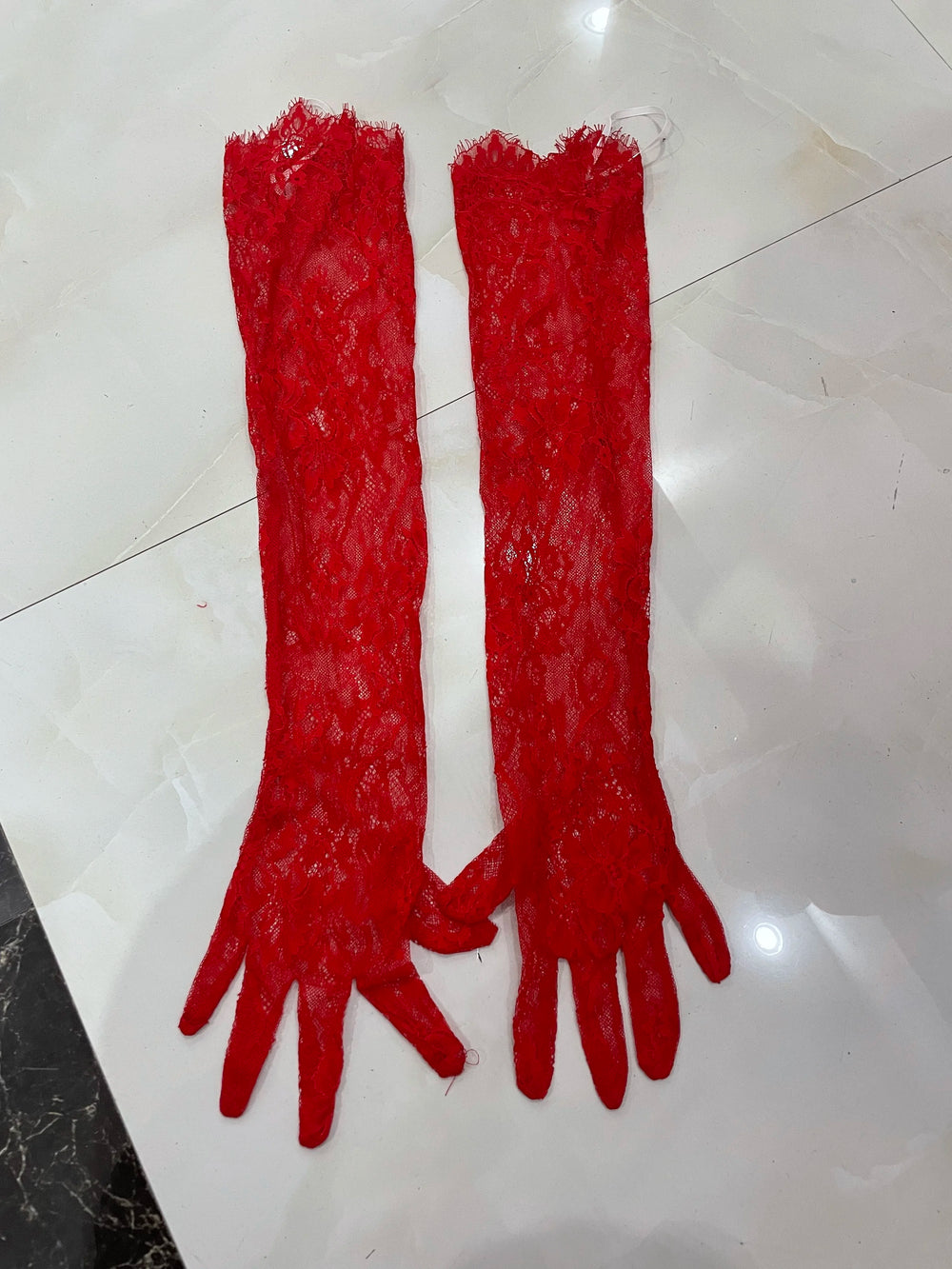 Pair of red lace gloves on a white tiled floor