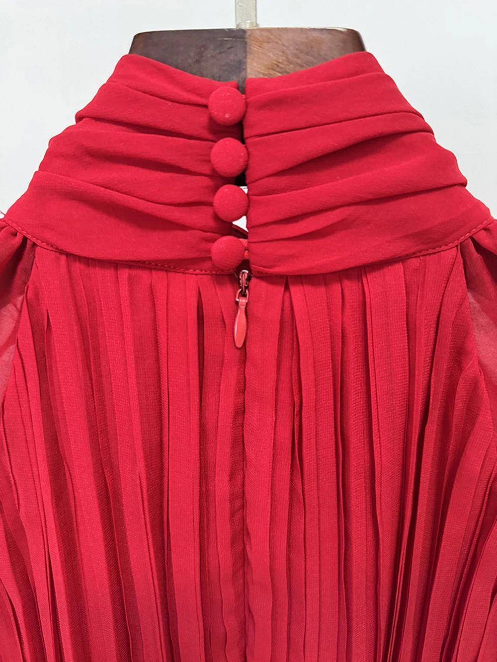 Red pleated dress with button details on a mannequin against a white background