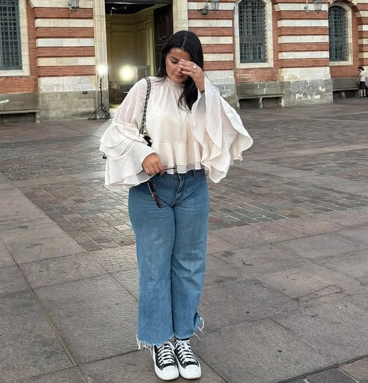 Person wearing a white blouse, blue jeans, and black sneakers in an urban setting.