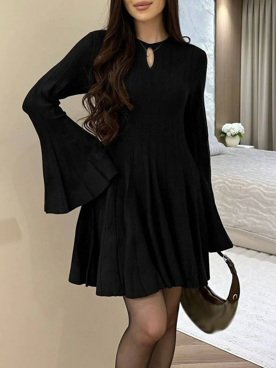 Woman wearing a black dress with flared sleeves in a bedroom setting