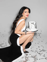 Woman in a black and white dress holding a cake with a white background