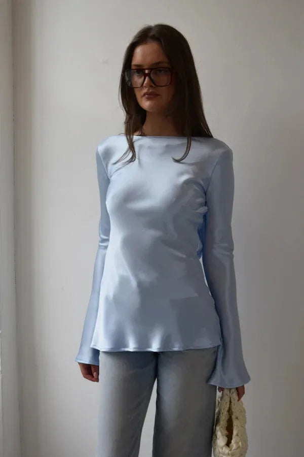 Woman wearing a light blue long-sleeve top and gray pants against a plain background