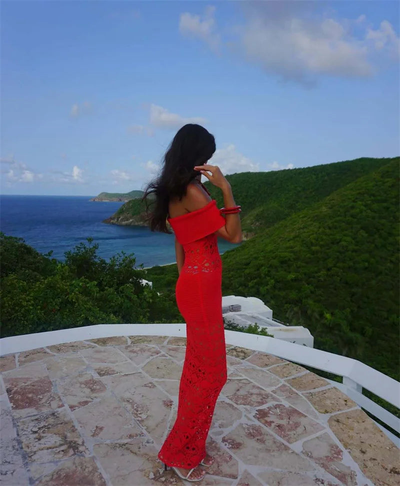 Woman in a red dress standing on a stone platform overlooking a scenic view of the ocean and mountains.