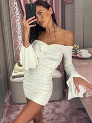 Woman in a white off-shoulder dress taking a mirror selfie in a room with pink decor.