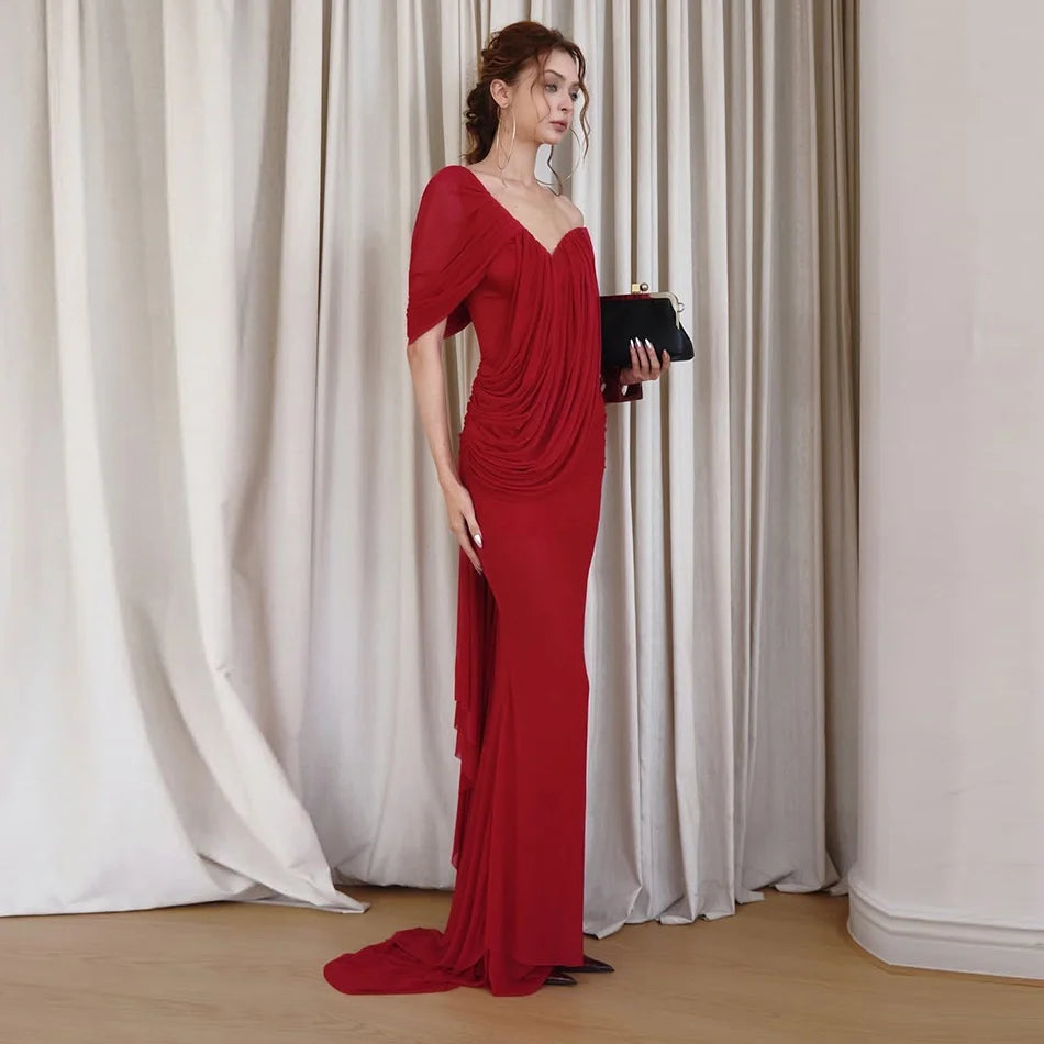 Model wearing a red draped one-shoulder dress with a clutch