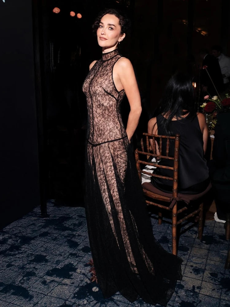 Woman in a black lace evening gown standing in a dimly lit room.