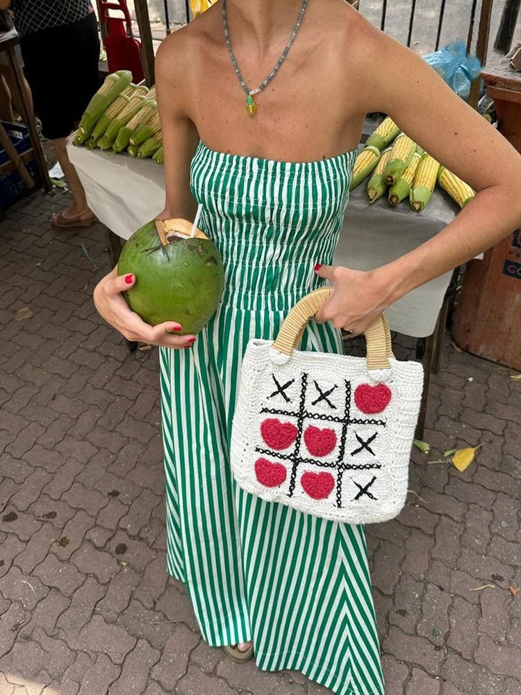 Woman in a green and white striped dress holding a coconuts and a woven bag with a tic-tac-toe pattern.