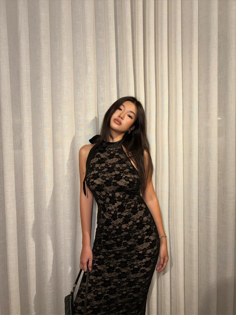 Woman in a black lace dress standing against a white curtain