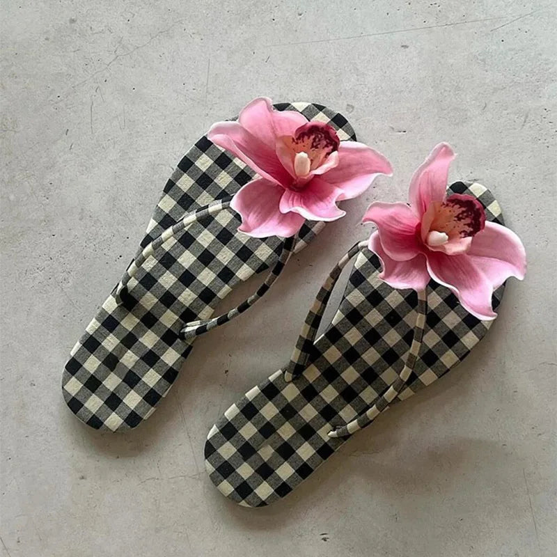 Pair of checkered flip-flops with pink floral decorations on a gray surface