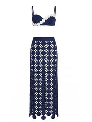 Product flat lay of a blue bikini top with white scalloped trim and a matching blue maxi skirt with geometric cut-outs.